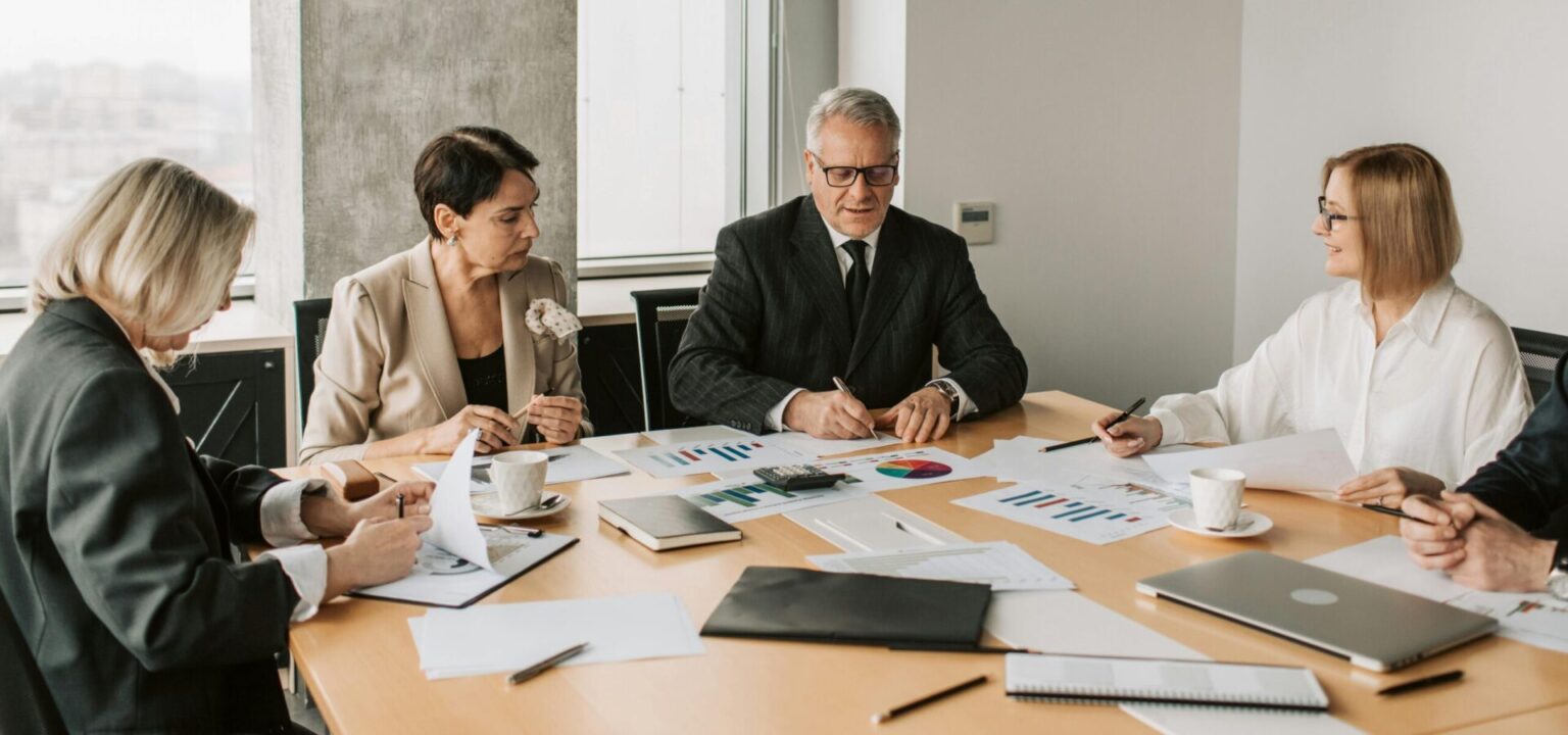 A group of professionals discussing business documents during a meeting in a modern office setting.