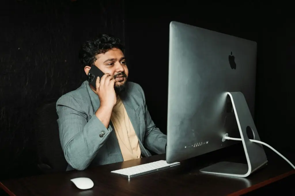Professional man multitasking at office desk using computer and smartphone.