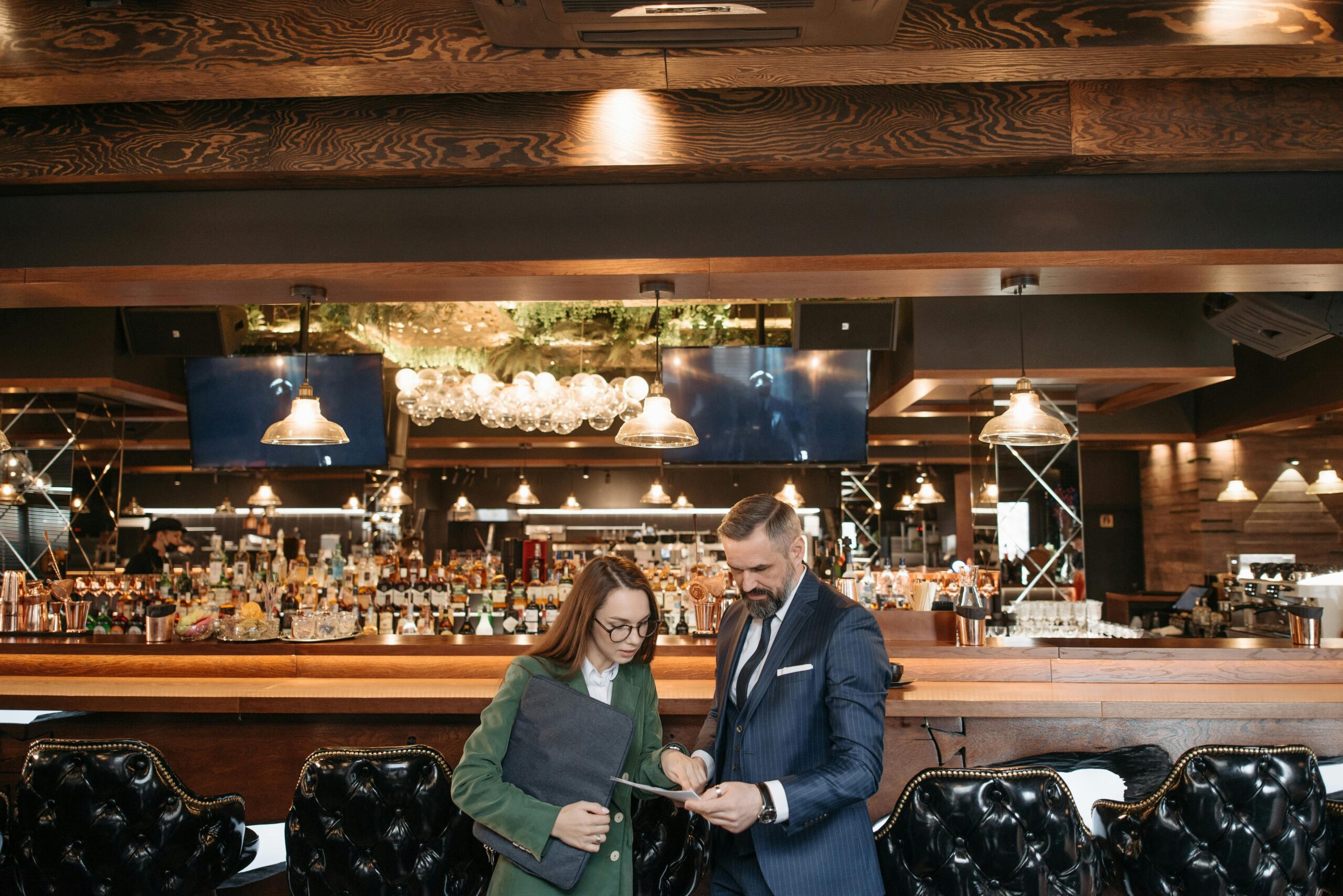 Professional man and woman discussing business documents in a stylish bar interior.